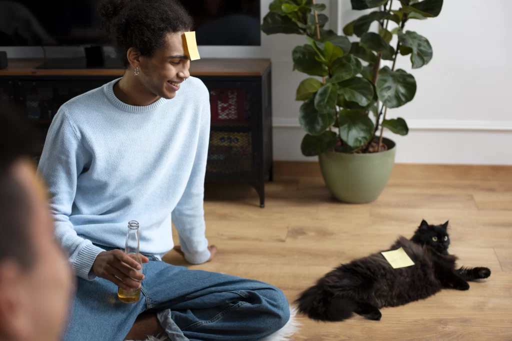 Gato negro recostado en el suelo con un papel adhesivo pegado en su cuerpo. A su lado, su dueño porta el mismo papel adhesivo.