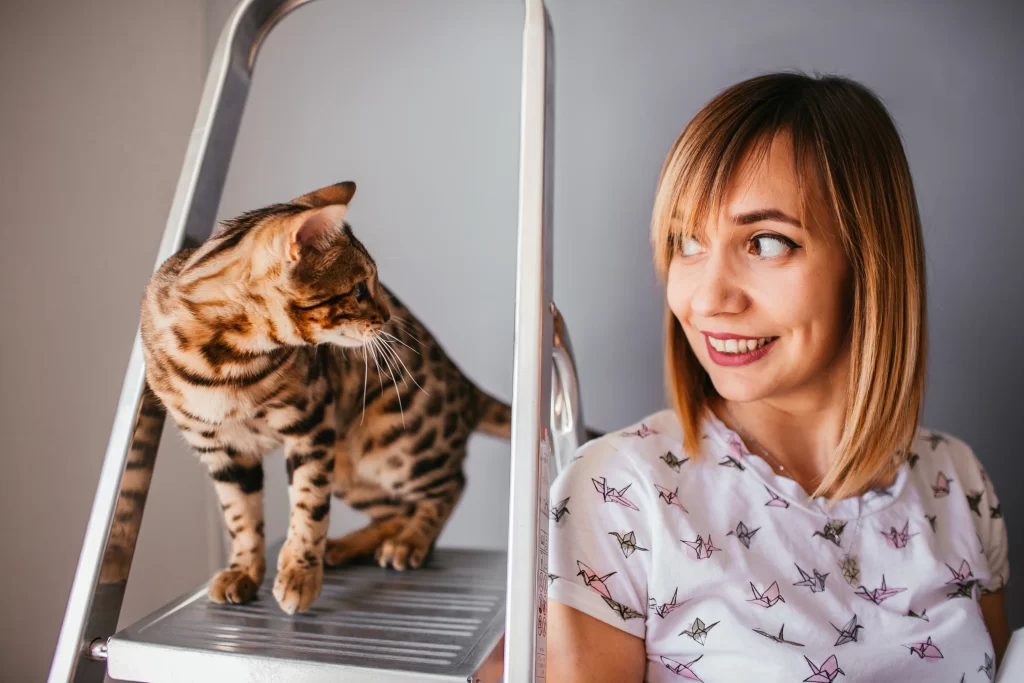 Gato sobre una escalera de metal mirando a su dueña, que, de espaldas, le devuelve la mirada.